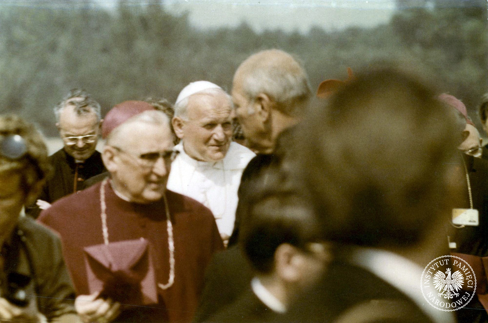 Jan Paweł II pośród duchownych i reporterów na płycie lotniska w Gębarzewie k. Gniezna. Pierwszy z lewej w okularach ceremoniarz papieski ksiądz Virgilio Noe. Fot. AIPN (Sygnatura: IPN Gd 1076/227)