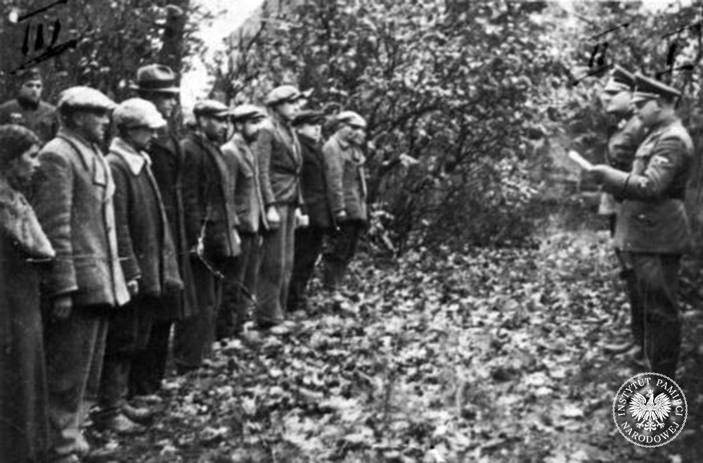 Szubin, 21 października 1939 r. Tuż przed egzekucją. Dwóch oficerów SS (jeden z nich to SS-Sturmbannführer Ernest Tiedemann) odczytuje wyrok śmierci grupie Polaków (fot. z zasobu IPN)