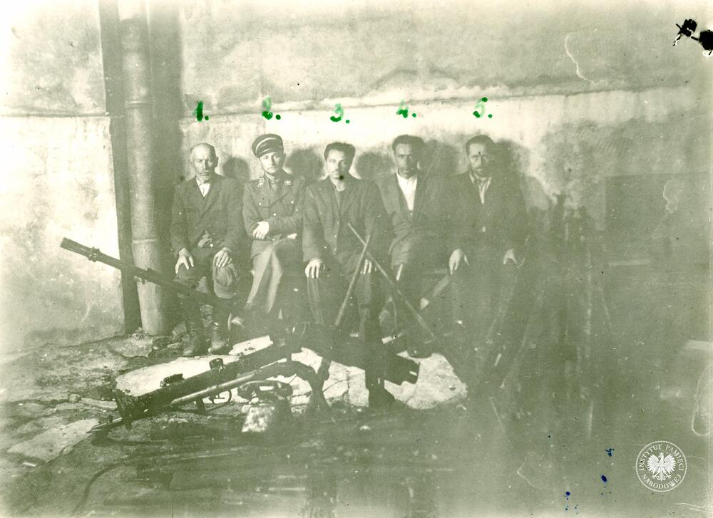 Tadeusz Gryblewski vel Tadeusz Wirecki ps. Kordian, Ostoja (1), Werfel – gajowy, magazynier broni (2), Piotr Woźniak ps. Wir (3), Franciszek Przysiężniak ps. Ojciec Jan (4), Ludwik Więcław ps. Śląsk (5). Przed więźniami, rzucone na stertę uzbrojenie i sprzęt wojskowy zdobyty w walce z oddziałami podziemia., fot. AIPN, sygn. IPNBU-3-3-30-1-1