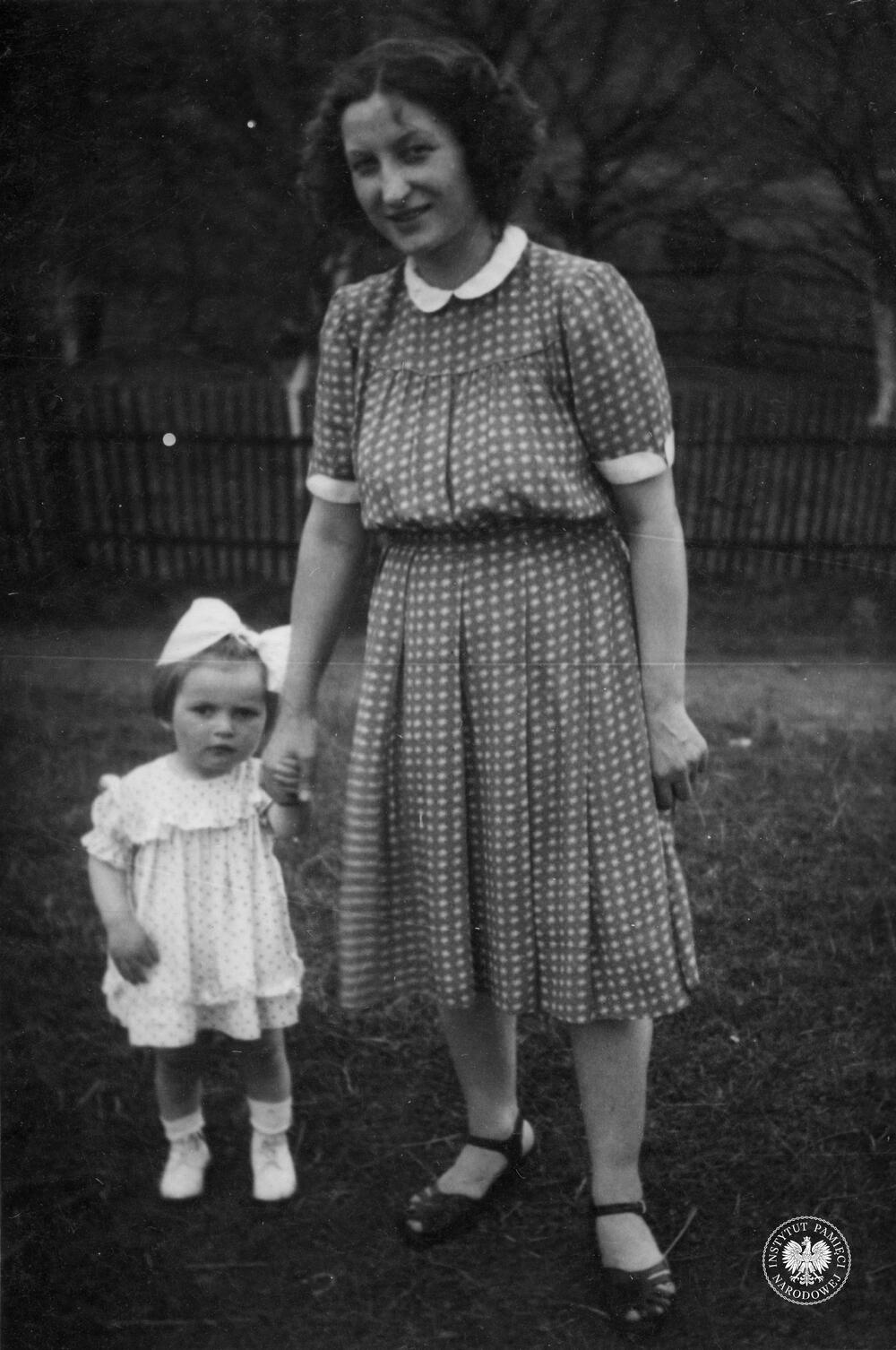 Na wiejskim podwórku stoi Jadwiga Wyżga. Kobieta trzyma za rękę swoją kilkuletnią córeczkę, fot. AIPN, sygn. IPNKr-10-1-4-2-1