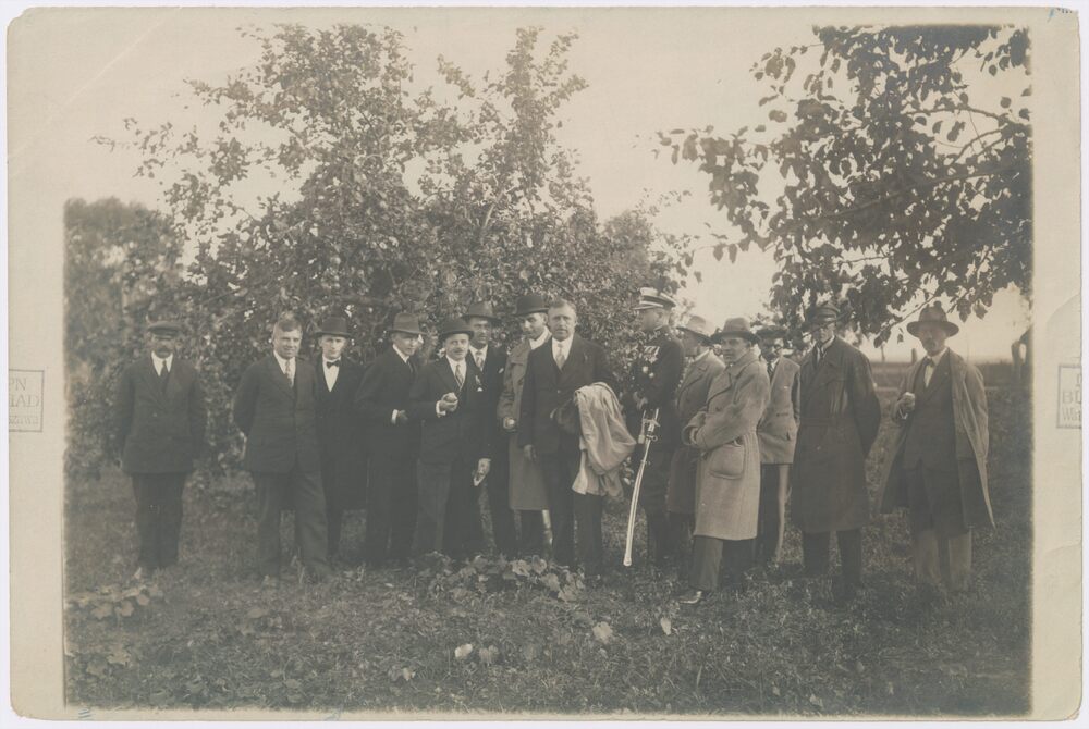 Grupa 14 urzędników, funkcjonariuszy i pracowników Urzędu Wojewódzkiego w Białymstoku wizytuje wzorcowe gospodarstwo sadownika o nazwisku Czarnowski we wsi Srebrowo w ówczesnej gminie Borzejewo. 5 od lewej, z jabłkiem w dłoni, stoi wojewoda białostocki Marian Zyndram-Kościałkowski. Fot. Domena publiczna, Źródło: AIPN, Sygnatura: IPNBU-1-3-3-2