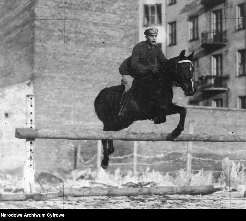 Porucznik Adam Królikiewicz, skacze przez przeszkodę podczas zawodów hippicznych 1 Pułku Szwoleżerów Józefa Piłsudskiego. W tle kamienica przy ul. Czerniakowskiej 159. Fot. NAC