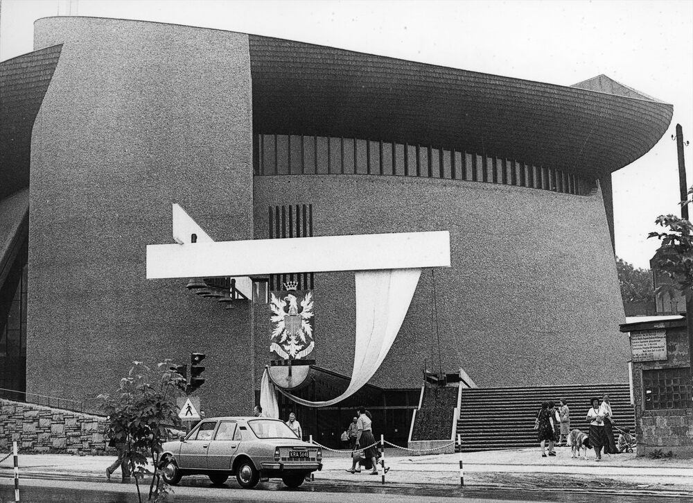 Widok z ulicy na kościół Arka Pana. Przy carillon (w centrum) zawieszony jest wielki szyld z Orłem w koronie. Na piersi orła tarcza z krzyżem i literą "M" pod jednym z ramion krzyża. Pod orłem napis: "HABEMUS PAPAM" [z łac. "Mamy papieża"]. Fot. AIPN