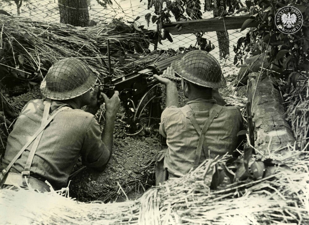 Polscy żołnierze piechoty na zamaskowanym stanowisku, obsługujący ciężki karabin maszynowy (7,69 mm Vickers Mk I na podstawie Mk IVB) – po lewej celowniczy, po prawej ładowniczy (trzymający taśmę z nabojami). Prawdopodobnie Ankona, lipiec 1944 r. Fot. z zasobu IPN