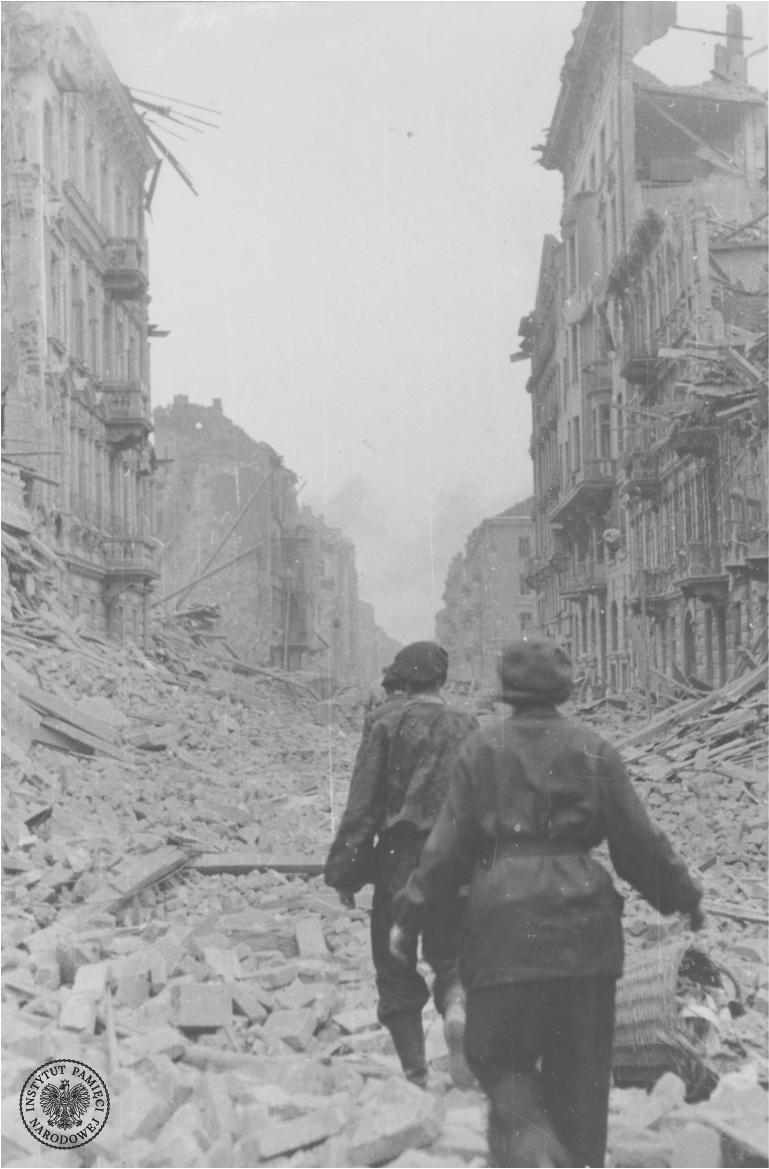 Zniszczone w czasie walk budynki przy jednej z ulic. Na pierwszym planie grupa powstańców idąca szeregiem wśród gruzów. 1944 r. (AIPN)