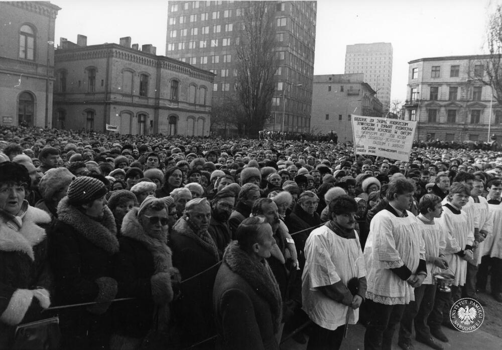 Na fotografii widać tłum zgromadzony pod kościołem. Zauważyć można transparent o treści: "Męczeńska śmierć ks. Jerzego wycisnęła trwałe i niezatarte piętno w sercach naszych. Niech ból ten przemieni się w nadzieję - wierność prawdzie, odwagę i męstwo. Zarząd pracownicy NSZZ Solidarność Ziemi Łódzkiej." (fot. AIPN)