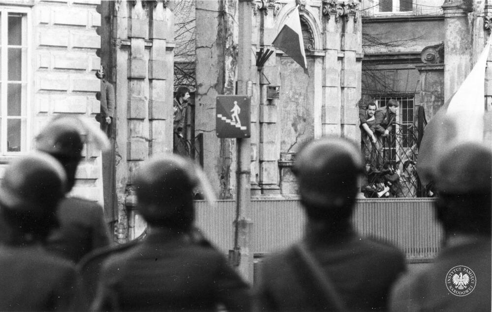 Manifestanci w Bramiej Głównej Uniwersytetu Warszawskiego na Krakowskim Przedmieściu 26/28. Na pierwszym planie funkcjonariusze Milicji Obywatelskiej, 3 maja 1982 r., z zasobu Archiwum IPN, sygn. IPNBU-11-5-13-187