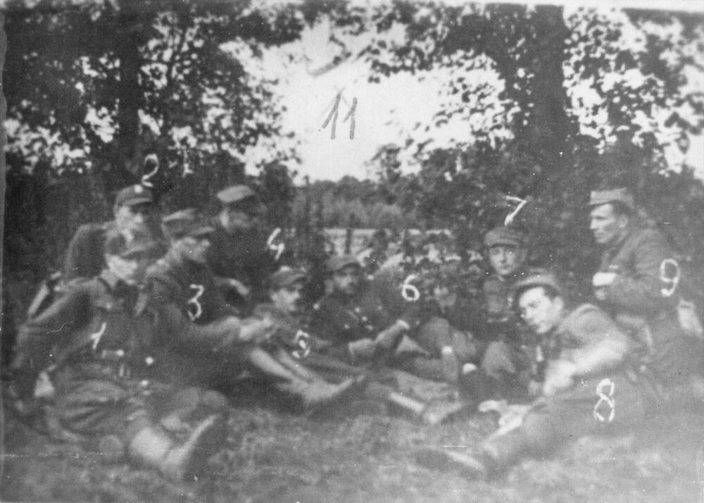 Kadra dowódcza V Wileńskiej Brygady AK od lewej: por. Mikołaj Kuroczkin ps. Leśny (nr 1), za nim (częściowo widoczny) ppor. Lucjan Minkiewicz ps. Wiktor (nr 2), ppor. Jerzy Jezierski ps. Stefan (nr 3), por. Zygmunt Błażejewicz ps. Zygmunt (nr 4), leży por. Marian Pluciński ps. Mścisław (nr 5), leży mjr Zygmunt Szendzielarz ps. Łupaszka (nr 6), ppor. Władysław Łukasiuk ps. Młot (nr 7), leży ppor. Romuald Rajs ps. Bury (nr 8), klęczy ppor. Jan Zaleski ps. Zaja (nr 9). Fot. AIPN