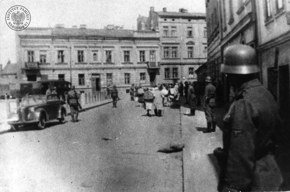 Likwidacja getta krakowskiego. Grupa Żydów (w głębi, na ulicy) zmierza prawdopodobnie w stronę obozu w Płaszowie. Na ostatnim planie i po prawej – kamienice stojące przy placu Zgody (dziś plac Bohaterów Getta). Marzec 1943 r. (fot. z zasobu AIPN)