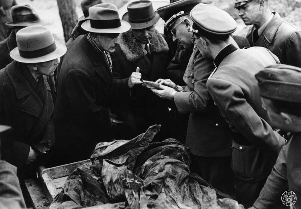 Ekshumacje zamordowanych przez NKWD oficerów Wojska Polskiego w Katyniu, kwiecień 1943. Na stole leżą zwłoki ofiary mordu katyńskiego. Komisja ekshumacyjna przegląda dokumenty znalezione przy ciele ofiary. Dokumenty trzyma w ręku prof. Gerhard Buhtz (w mundurze, czwarty z prawej). Fot. z zasobu IPN