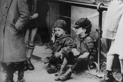 Dwoje dzieci żydowskich siedzi na ulicy w getcie. Warszawa, 1940-1942 r. (fot. z zasobu IPN, sygn. GK-8-3-17-116)