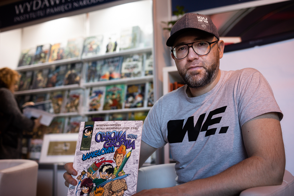 Hubert Ronek, twórca komiksowej serii IPN „Wojenna odyseja Antka Srebrnego” oraz „Aga, Adam i Hamlet na tropie tajemnic” rysuje i podpisuje – Targi Wydawców Katolickich w Warszawie, 23 kwietnia 2023. Fot. Sławek Kasper.