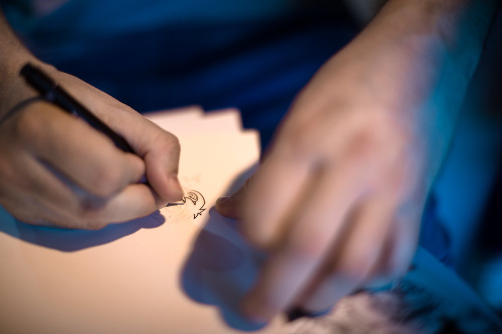 Hubert Ronek, twórca komiksowej serii IPN „Wojenna odyseja Antka Srebrnego” oraz „Aga, Adam i Hamlet na tropie tajemnic” rysuje i podpisuje – Targi Wydawców Katolickich w Warszawie, 23 kwietnia 2023. Fot. Sławek Kasper.