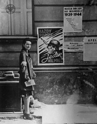 Łączniczka przy plakacie autorstwa Henryka Chmielewskiego „Każdy pocisk jeden Niemiec”; Warszawa, sierpień 1944 r. Autor: Eugeniusz Lokajski (fot. z zasobu IPN)