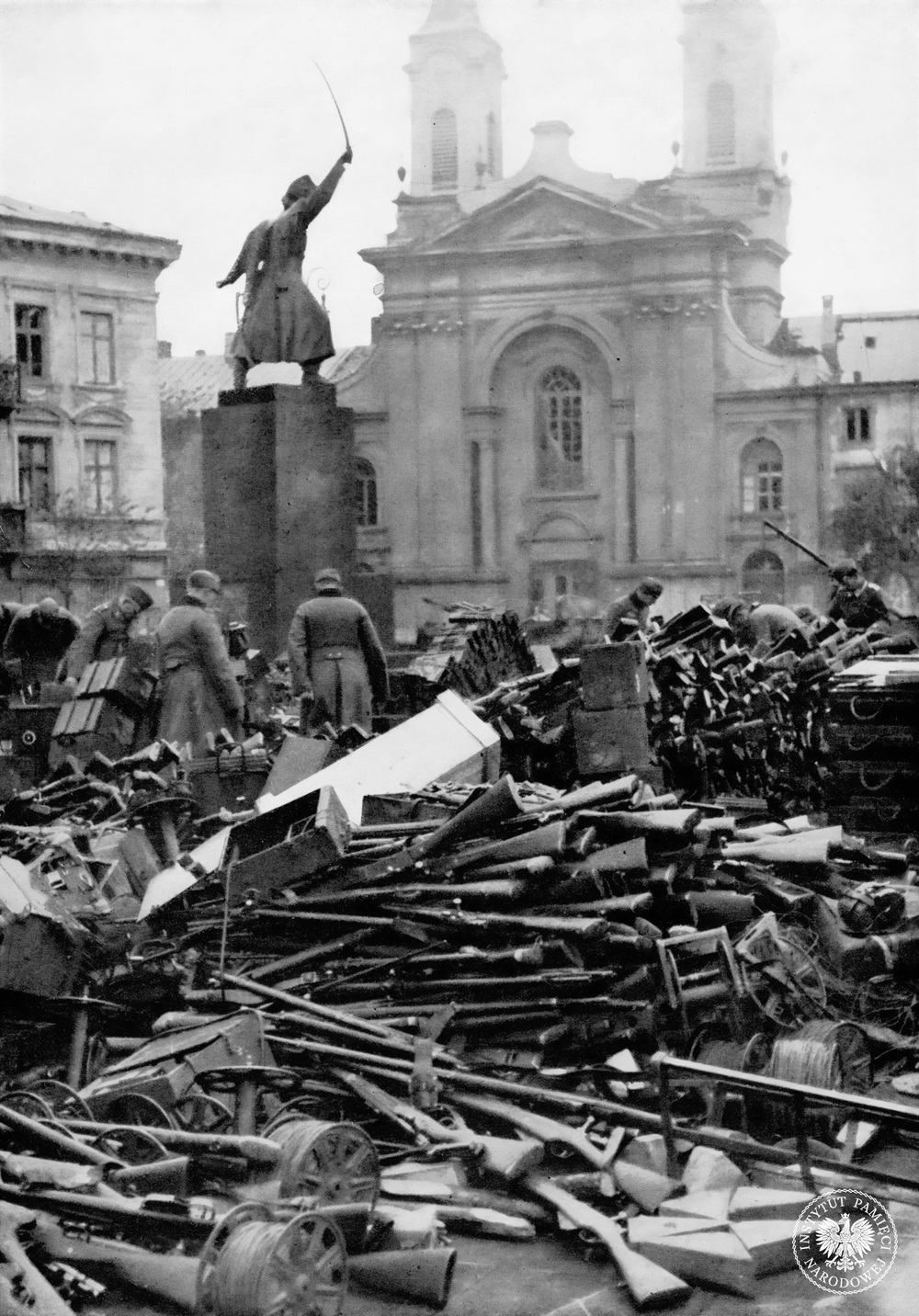 Żołnierze niemieccy wśród stert broni oddziałów polskich zgromadzonej na placu Krasińskich po kapitulacji Warszawy. Na pierwszym planie szpule kabli telefonicznych i karabiny, w głębi katedra polowa WP. Po lewej, widoczny od tyłu, pomnik Jana Kilińskiego. Jego uniesiona szabla i gest wezwania do walki w tych okolicznościach miały szczególną wymowę. Warszawa, październik 1939 r. (fot. z zasobu AIPN)